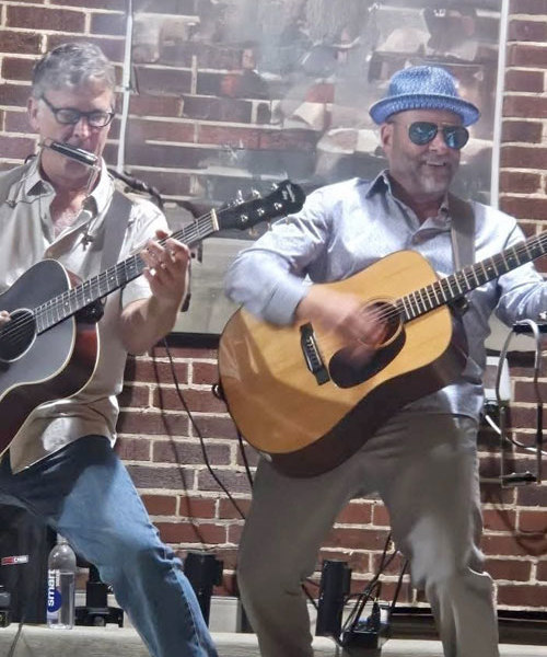 Mike Lenz and Tony Paparella onstage, both playing acoustic guitars, lunging forward, big smiles.