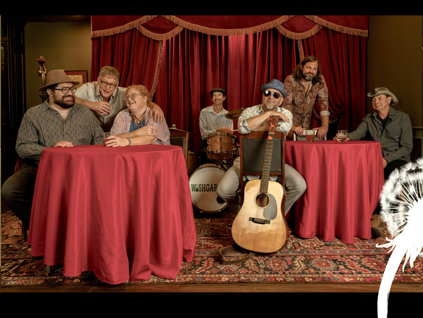 Wishgarden band at round tables with red tablecloths in front of ornately curtaned stage with big smiles.