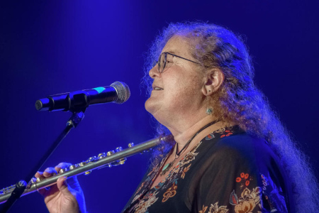 Wishgarden member Saam Cabot with flute onstage, at mic, singing.