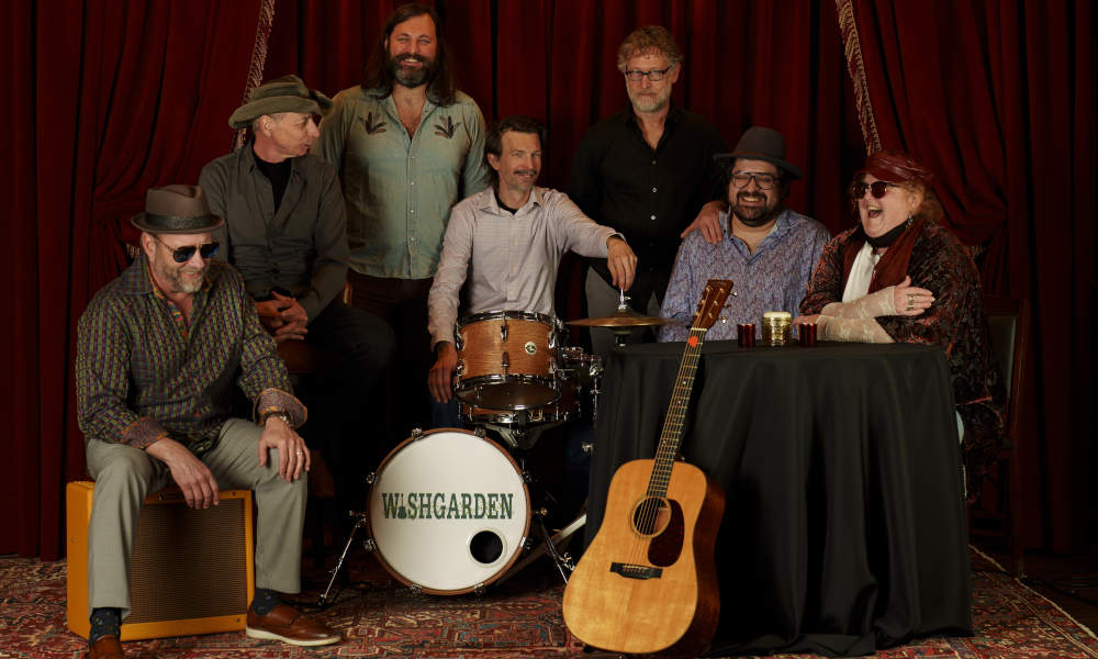 CD Release Party concert. Sevensmiling members of Wishgarden Band gathered around a table with Wishgarden on drumkit, and an acoustic guitar.